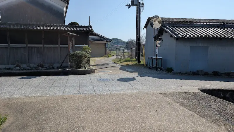 明日香村の民家が立ち並ぶ細い生活道路。車一台がやっと通れる道幅で、見通しの悪いカーブミラーが設置されている様子。