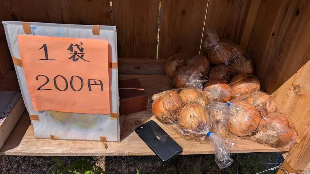 明日香村の無人販売所で売られている玉ねぎ。iPhone SEを隣に置くことで、1袋あたりのボリュームがわかるようになっている。