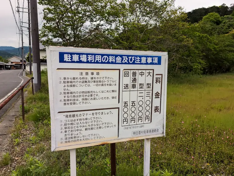 明日香村駐車場連絡会による有料駐車場の料金表看板。普通車500円、中型2,000円、大型3,000円の料金と、飛鳥観光のマナー(ゴミ持ち帰り、田畑への立ち入り禁止など)が記載されている。