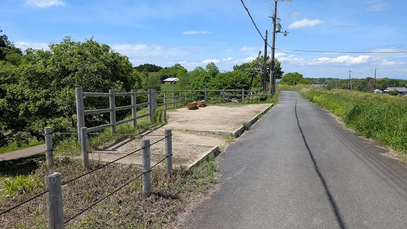 明日香村の歴史的な風景の中にある、平坦でまっすぐな散策路。道沿いには木製の柵で囲まれた休憩スペースが設置されている。