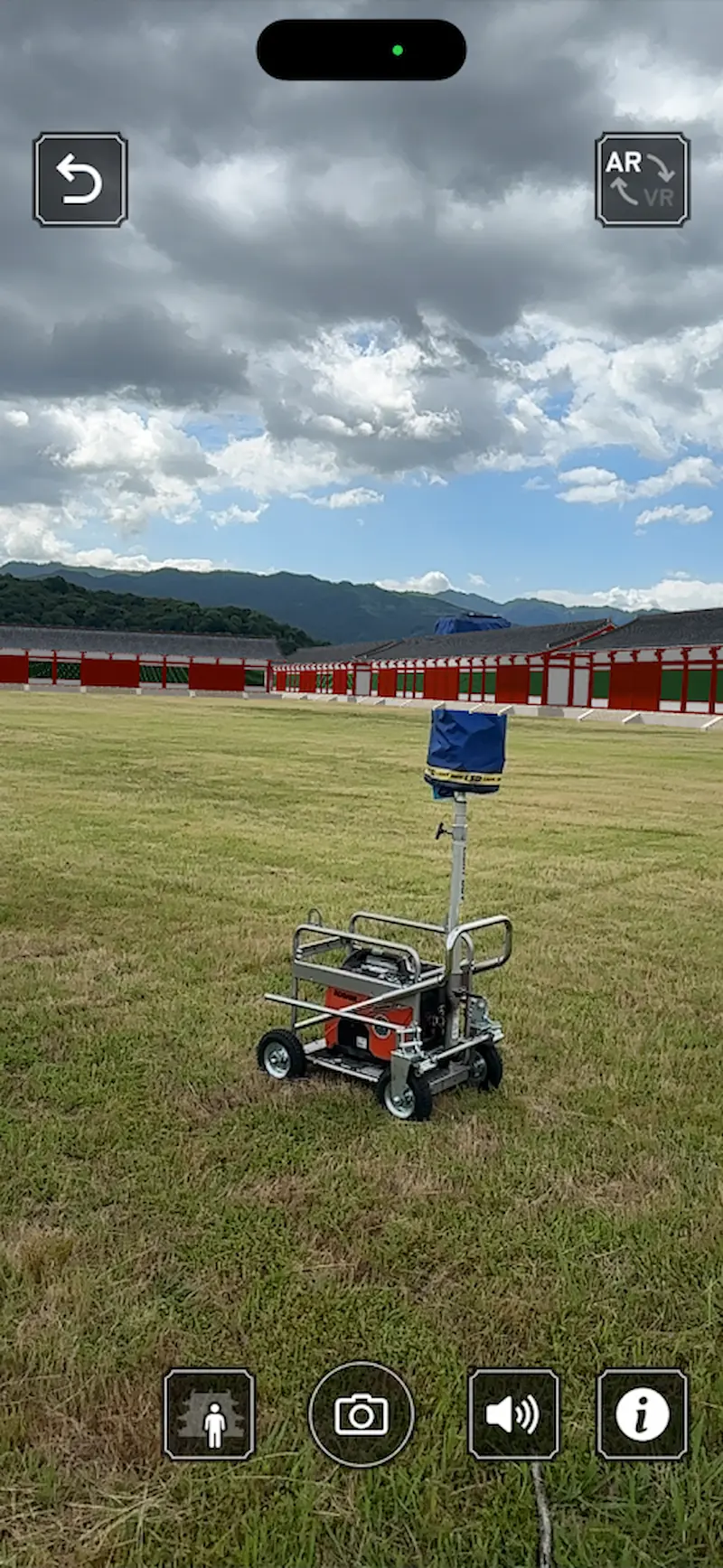 藤原宮跡にて「XR藤原宮」アプリのARモードを使用し、現在の広大な敷地に当時の赤い回廊を重ねて表示している様子。
