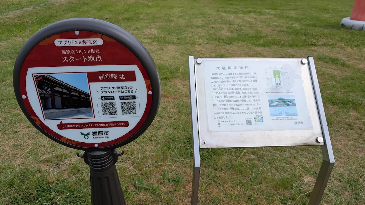 藤原宮跡にある「XR藤原宮」アプリのAR/VR復元スタート地点を示す標識と、大極殿院南門についての解説板。