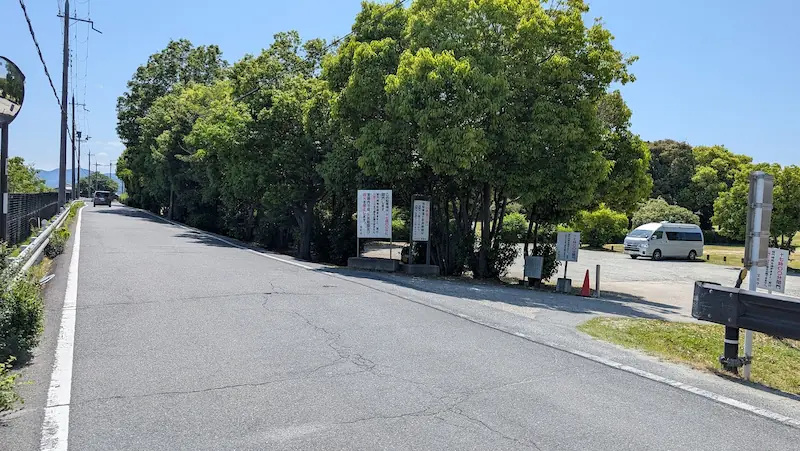藤原宮跡周辺の道路沿いにある、未舗装で砂利敷きの臨時駐車場2。入り口に複数の案内看板が設置されている様子。