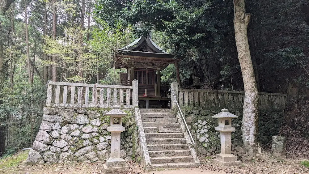 高い石垣の上に建てられた葛城水分神社の木造本殿。手前には石段と一対の石灯籠があり、周囲を深い森が囲んでいる。