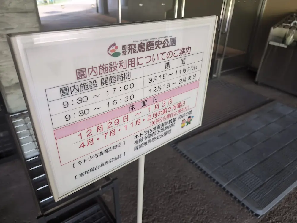 国営飛鳥歴史公園の開館時間と休館日を記載した案内板。季節による時間変更や定休日が明記されている。
