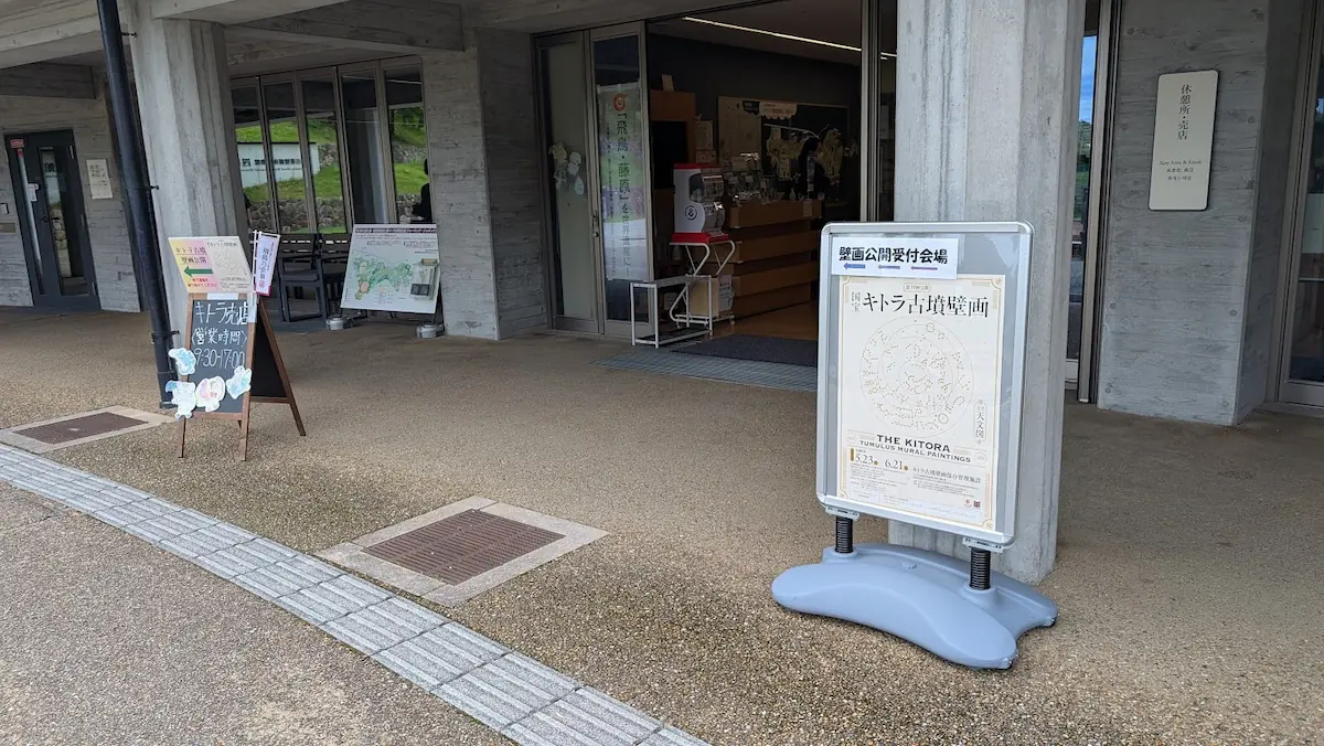キトラ古墳壁画体験館「四神の館」入口。国宝キトラ古墳壁画公開の受付会場であることを示す看板と、売店の営業案内ボードが設置されている様子。