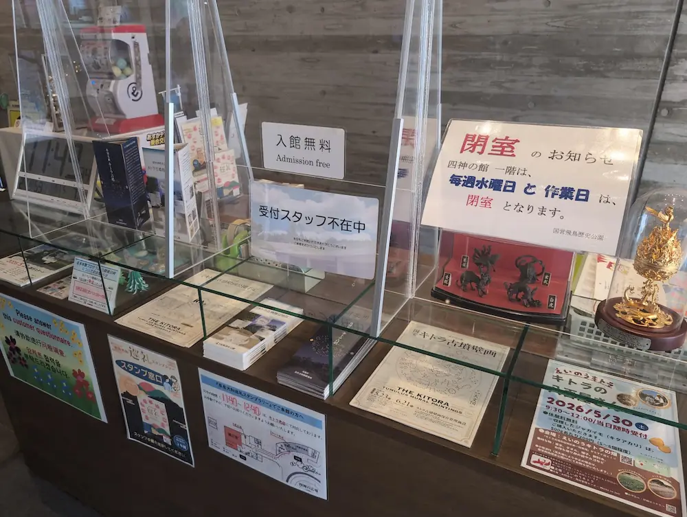 キトラ古墳壁画体験館「四神の館」の受付カウンター。入館無料の表示や、展示室の閉室日に関する案内が掲示されている。