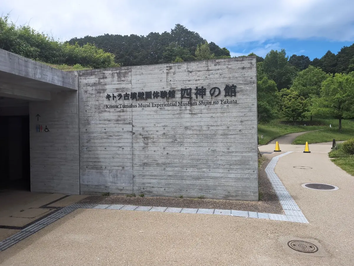 キトラ古墳壁画体験館「四神の館」の入り口。コンクリート壁に施設名が刻まれ、左手にはトイレの案内看板がある。
