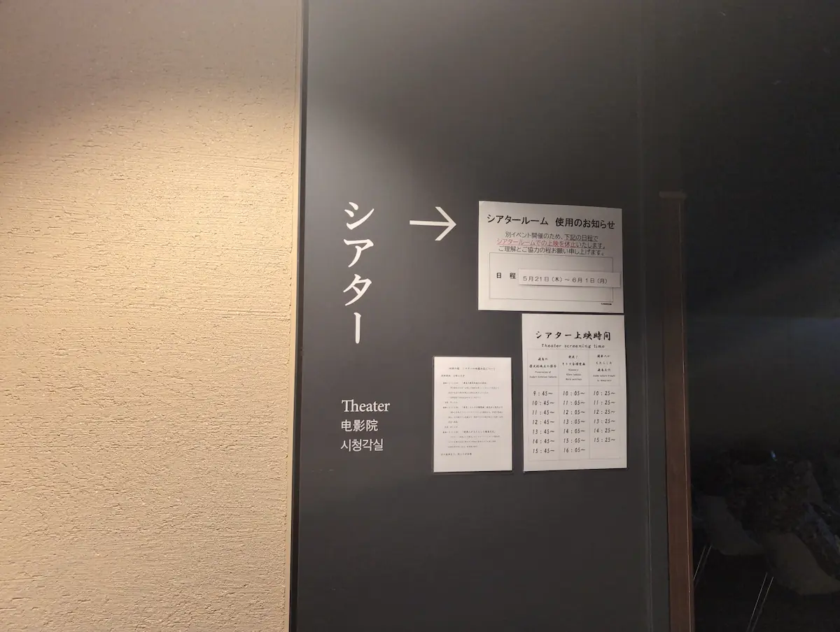 四神の館シアタールームの案内看板。上映時間の一覧と、イベント開催による上映休止期間の注意書きが掲示されている。