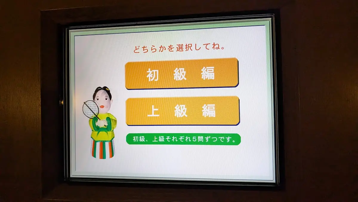 万葉文化館内のデジタルクイズ端末の画面。「初級編」「上級編」の選択ボタンがあり、左側には万葉時代の衣装を着たキャラクターが描かれている。
