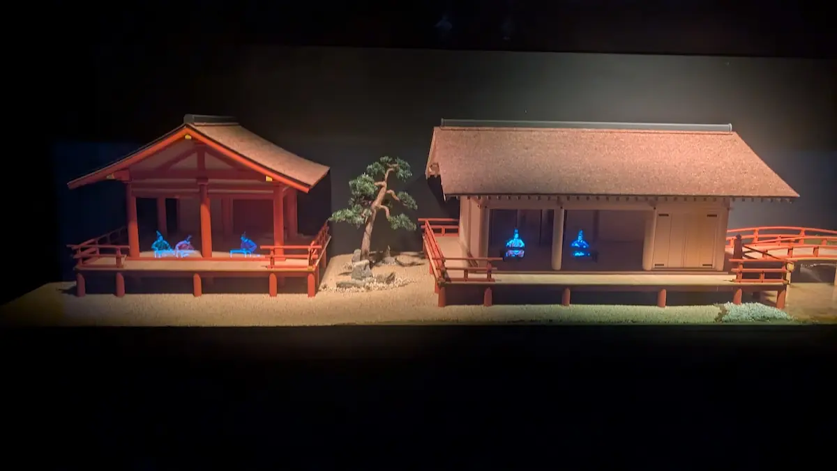 万葉文化館の展示模型。ボタン操作により、二つの日本建築の模型の中に、青い光を放つ人物のホログラムが映し出されている様子。