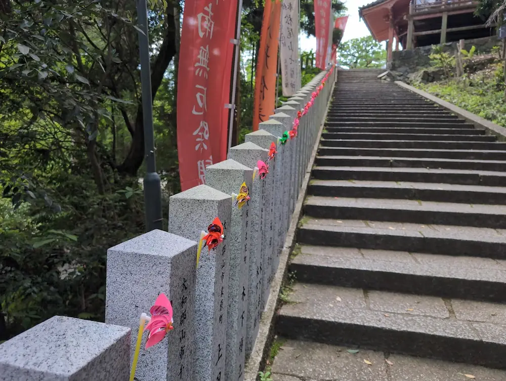 松尾寺の石段の手すりに飾られた色鮮やかな風車。参道に並ぶ旗と共に、本堂へ続く道を彩っている。