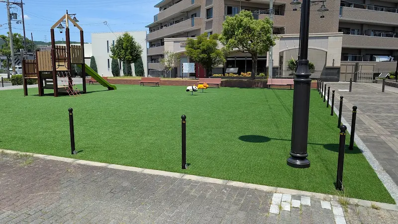 二上駅前北広場の遊具エリア。人工芝の上に滑り台と、パンダとライオンの形をしたスプリング遊具が設置されている。