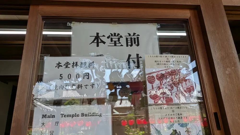 お房観音の本堂前受付のガラス窓に貼られた案内。本堂拝観料が500円（境内は無料）であることや、提灯まつり期間限定の御朱印（800円）、メダカの絵入り御朱印（800円）の見本が掲示されている。