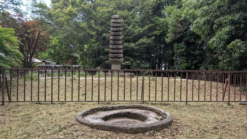 於美阿志神社の境内に立つ、重要文化財の十三重石塔。柵で囲われた周囲と、手前に円形の石造遺構がある様子。