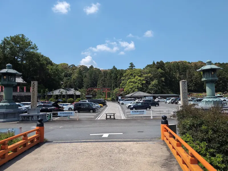 5月15日（金）午前10時半頃の霊山寺駐車場。平日にもかかわらず、バラ園の見頃に合わせて多くの車が停まっており、満車に近い状態。手前には朱色の橋、中央奥には鳥居が見える。