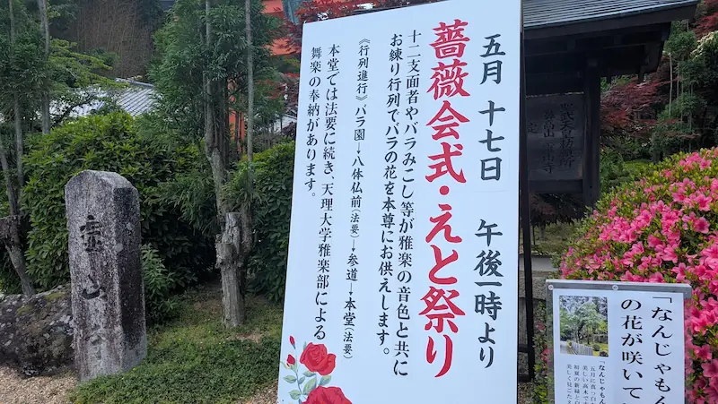 5月17日に開催される霊山寺の「薔薇会式・えと祭り」の案内看板。バラのみこしやお練り行列、天理大学雅楽部による舞楽の奉納などのスケジュールが記されている。