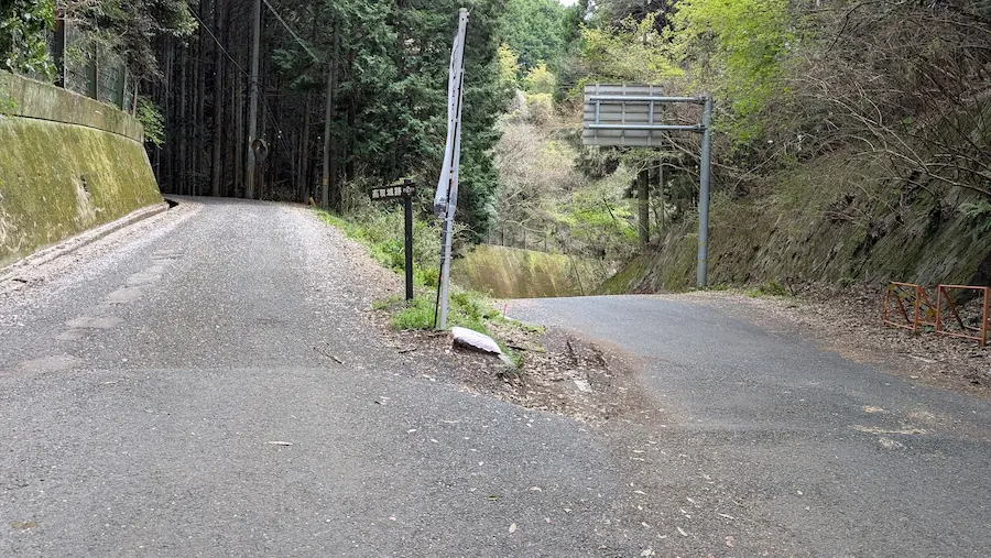 高取城跡へ向かう山道の分岐点。壺阪寺側から登ってきた道が二手に分かれ、左側の登り坂に「高取城跡」と書かれた小さな案内看板が立っている。右側の道は下り坂になっている。