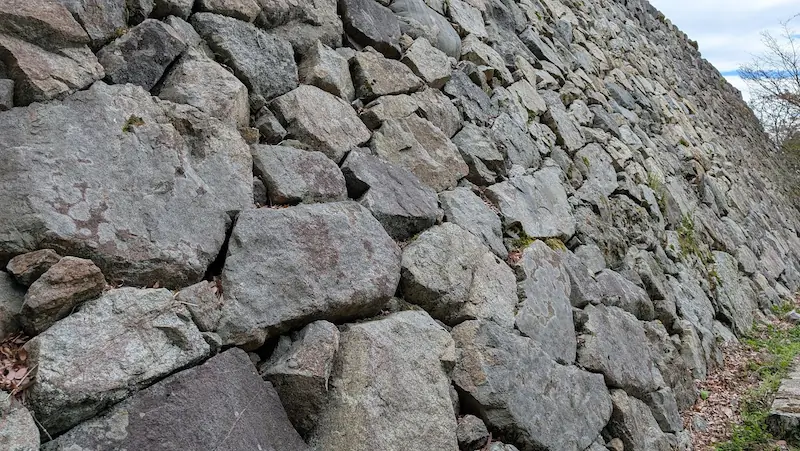 高取城跡の本丸付近にある巨大な高石垣の接写。不揃いな巨石が隙間なく積み上げられており、石の表面には歳月を感じさせる苔や模様がついている。斜め上方へ向かって力強く伸びる石積みの構図。