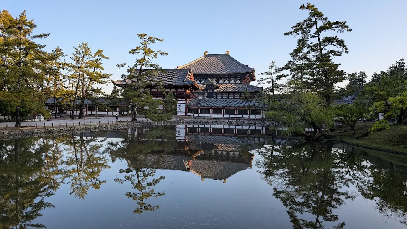 奈良公園・東大寺の鏡池。波一つない水面に、中門と背後の大仏殿、周囲の松の木が上下対称に美しく反射している景観。