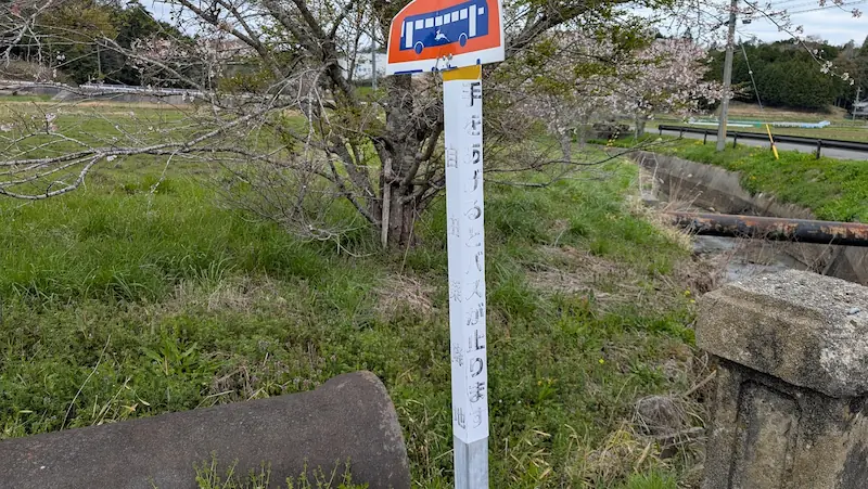 都祁水分神社のすぐ前にあるバス停の支柱。白い柱に「手をあげるとバスが止まります」と手書きで案内されており、上部には鹿のイラストが描かれたバスの標識がついている