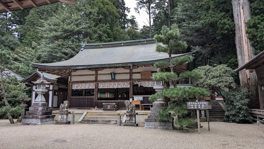 都祁水分神社の拝殿全景。木造の落ち着いた社殿の前に石灯籠や松の木が並び、背後には鬱蒼とした森が広がっている風景