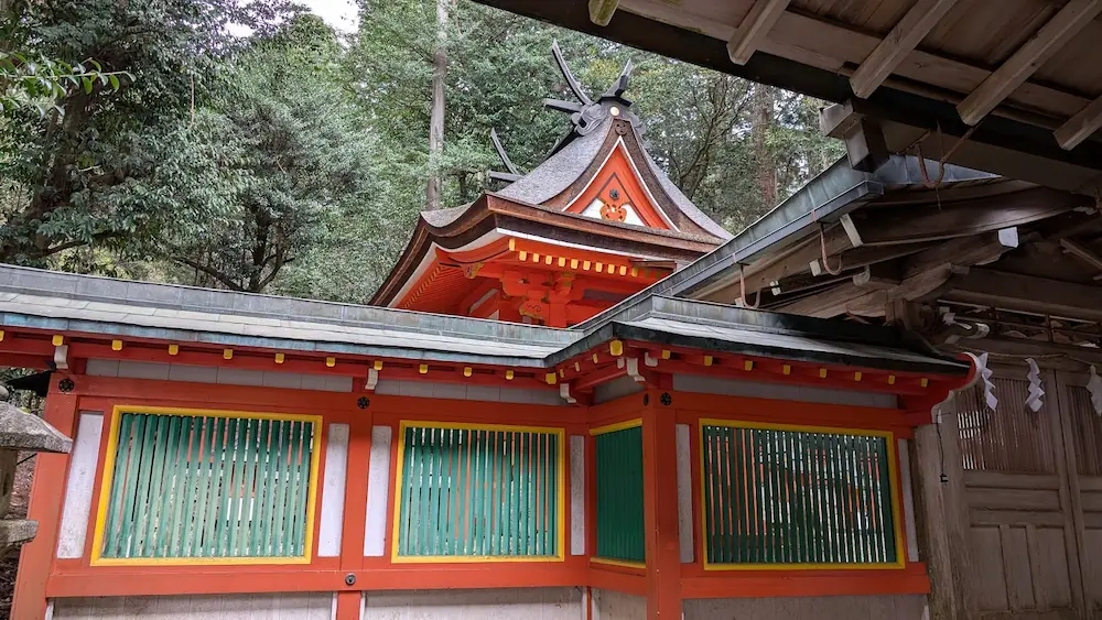 都祁水分神社の本殿を左斜め前方から見た風景。朱色の社殿と緑色の連子窓が並び、屋根の優美な曲線と背後の木々が調和している