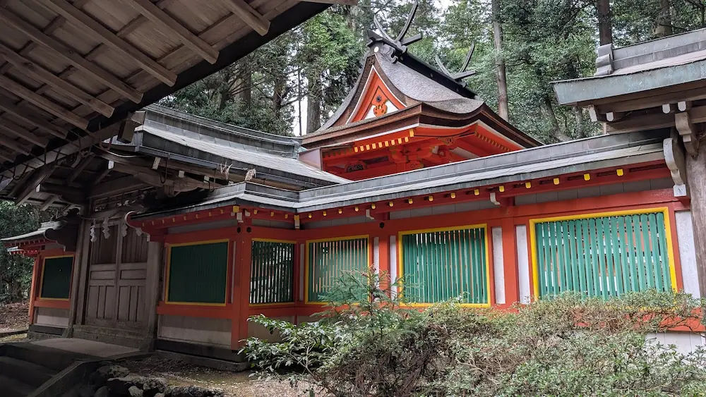 都祁水分神社の本殿。鮮やかな朱塗りの社殿と、緑色の連子窓（れんじまど）が特徴的な建物。背後には深い杉木立が広がっている