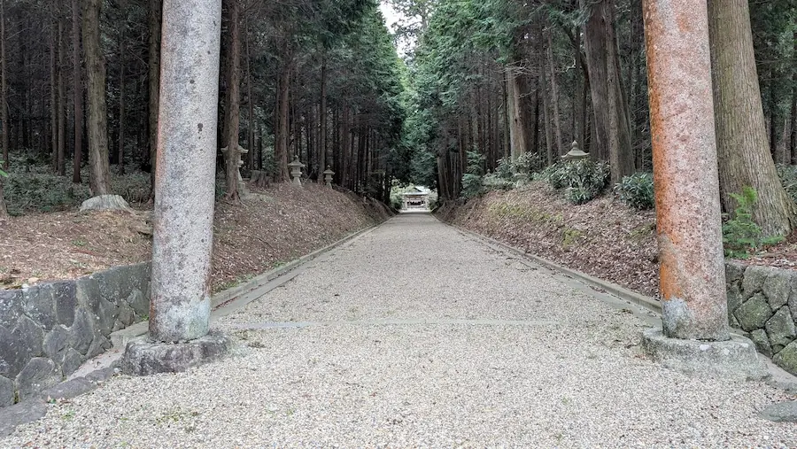 都祁水分神社の鳥居の間から見た真っ直ぐな参道。両脇には高くそびえる杉の木々が並び、静かな砂利道の先に拝殿が小さく見えている風景