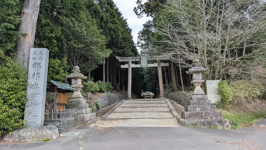 都祁水分神社の入り口。左側に「式内大社 都祁水分神社」と刻まれた大きな社標があり、正面には石造りの鳥居と深い森へと続く参道が見える風景
