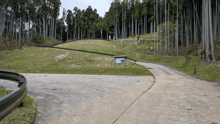 宇陀松山城跡の頂上まで残り約200m地点にある、コンクリート敷きの駐車場スペース。周囲は杉林に囲まれており、案内板が設置されている。