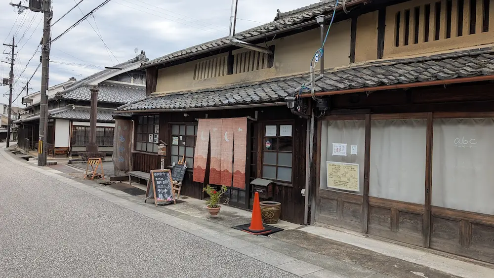 奈良県宇陀市松山地区にある、伝統的な古民家を改装したおしゃれなカフェの外観。茶色の暖簾が掛かり、店先にはランチやコーヒーのメニューボードが置かれている。