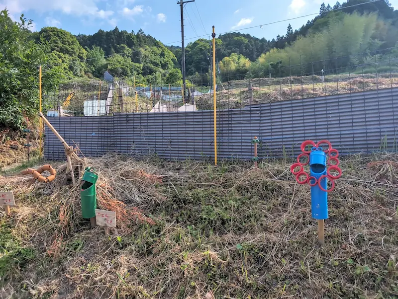 稲渕棚田の道端に設置された、パイプで作られたヘビとカエルと万博のキャラクターの手作り案山子