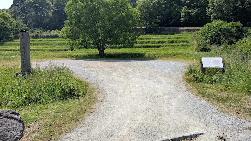 飛鳥稲渕宮殿跡の石碑と、奥に棚田が広がる砂利敷きの広場。案内看板が設置された史跡の全景。