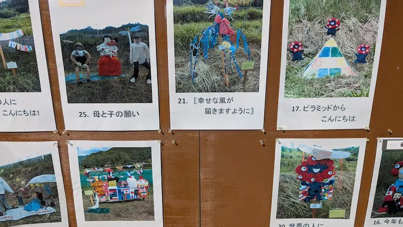 稲渕棚田の案山子コンテストの過去の入賞作品が掲示されたボード。母子の案山子やピラミッドなどの個性豊かな作品写真が並ぶ
