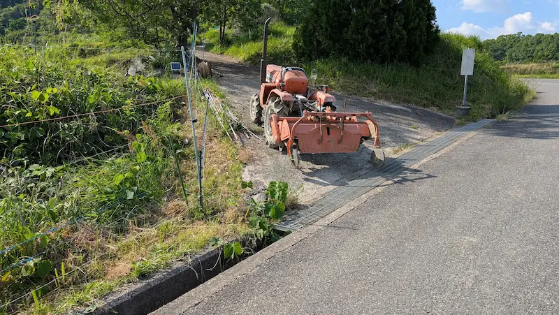 田植え前の準備で活躍する、明日香村の農道に停められたオレンジ色のトラクター。周囲の自然豊かな農村風景。