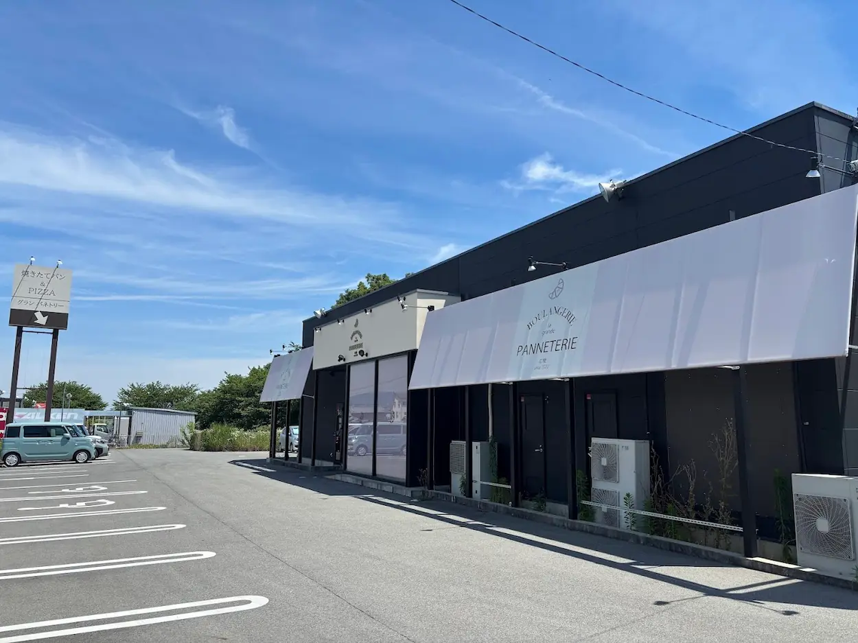 青空の下、モダンな黒い建物に白いオーニングが映えるグランパネトリー広陵店の外観と広々とした駐車場。