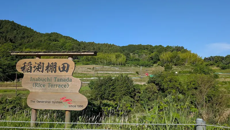 明日香村の稲渕棚田に設置された木製の看板。「稲渕棚田」の文字と棚田の風景が広がる様子。