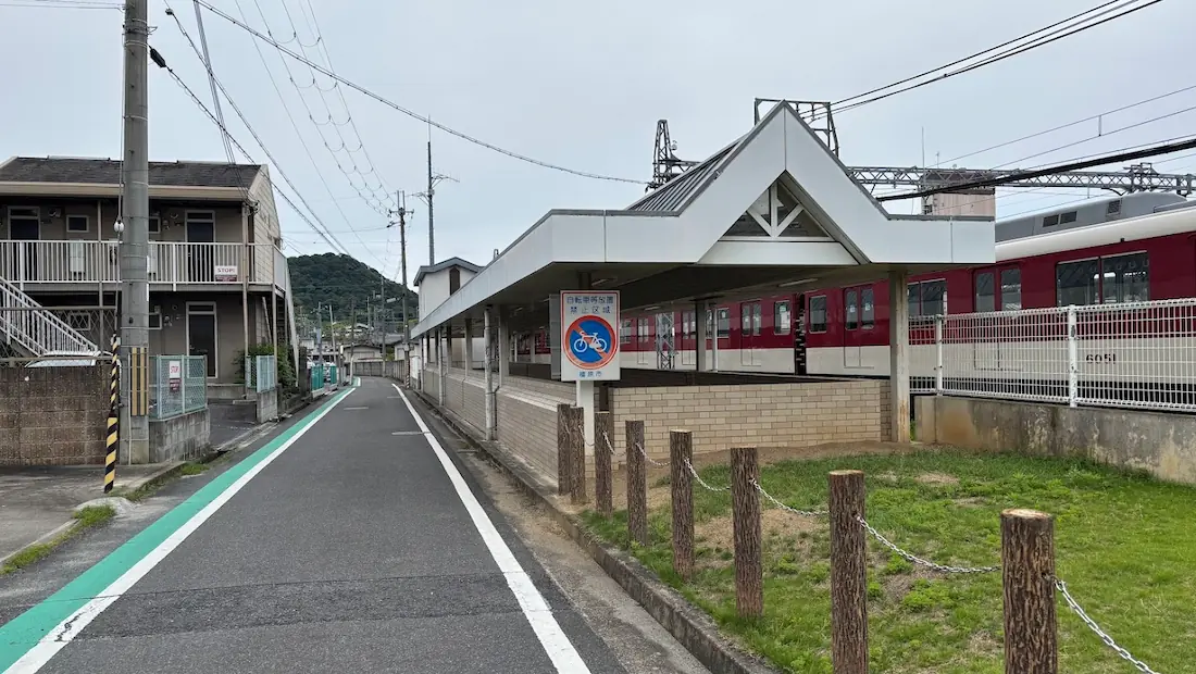 近鉄橿原神宮前駅西出口付近の線路沿いの道路。電車がすぐそばを走り、自転車禁止区域の看板がある狭めの道