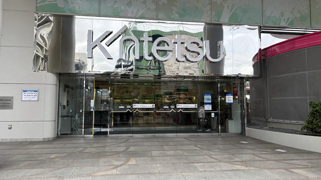 橿原市にある近鉄百貨店の正面入り口。ガラス張りの自動ドアの上に「Kintetsu」のロゴが掲げられている様子