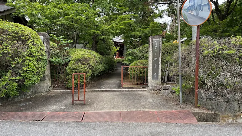 緑豊かな木々に囲まれた久米寺の入り口。石柱の寺号標と、奥へと続く参道が静かな雰囲気を作り出している