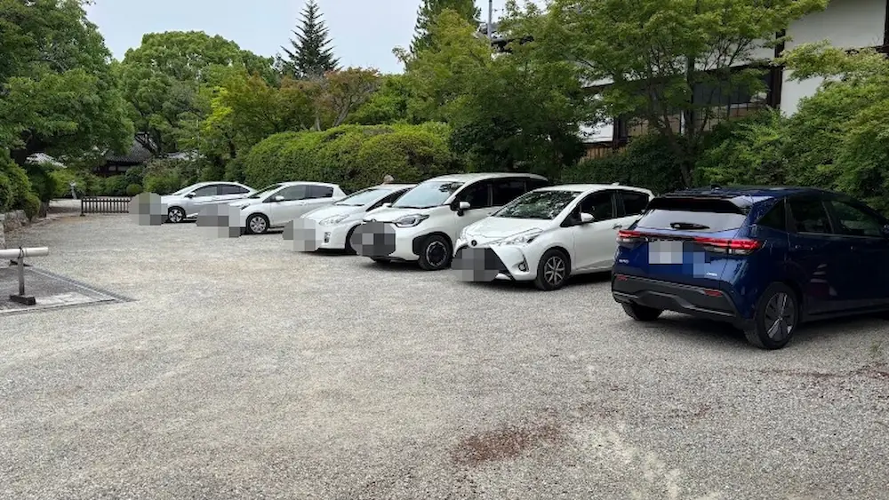 久米寺の駐車場。砂利敷きの平坦なスペースで、木々に囲まれた落ち着いた雰囲気の中、車がゆったりと停められている様子
