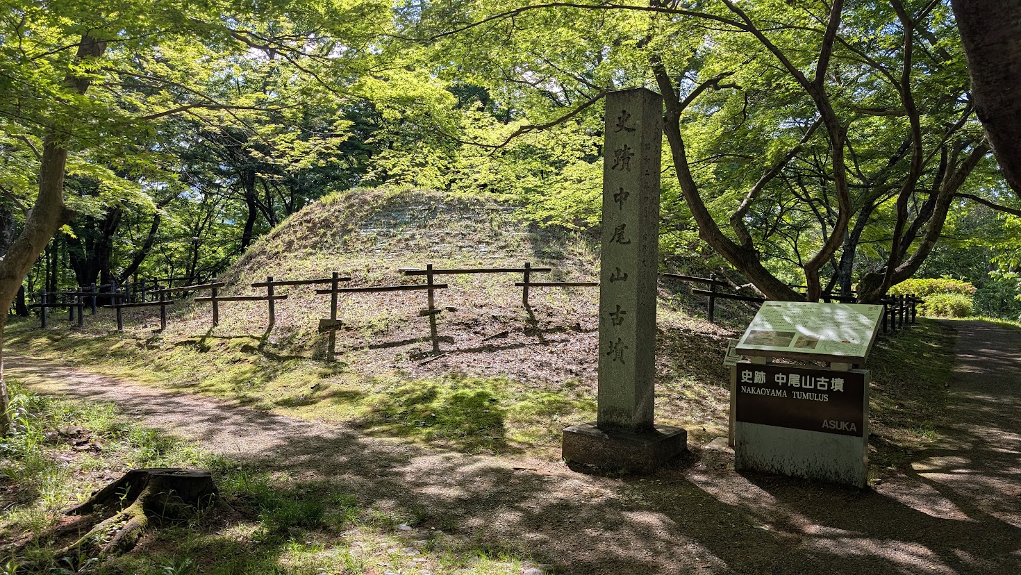 木々に囲まれた中尾山古墳の全景と、その手前に立つ石碑および史跡説明板