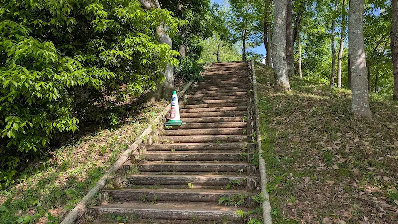 中尾山古墳へ続く、木枠で段差が作られた急な階段の様子。左側には「頭上注意」と書かれたコーンが置かれている