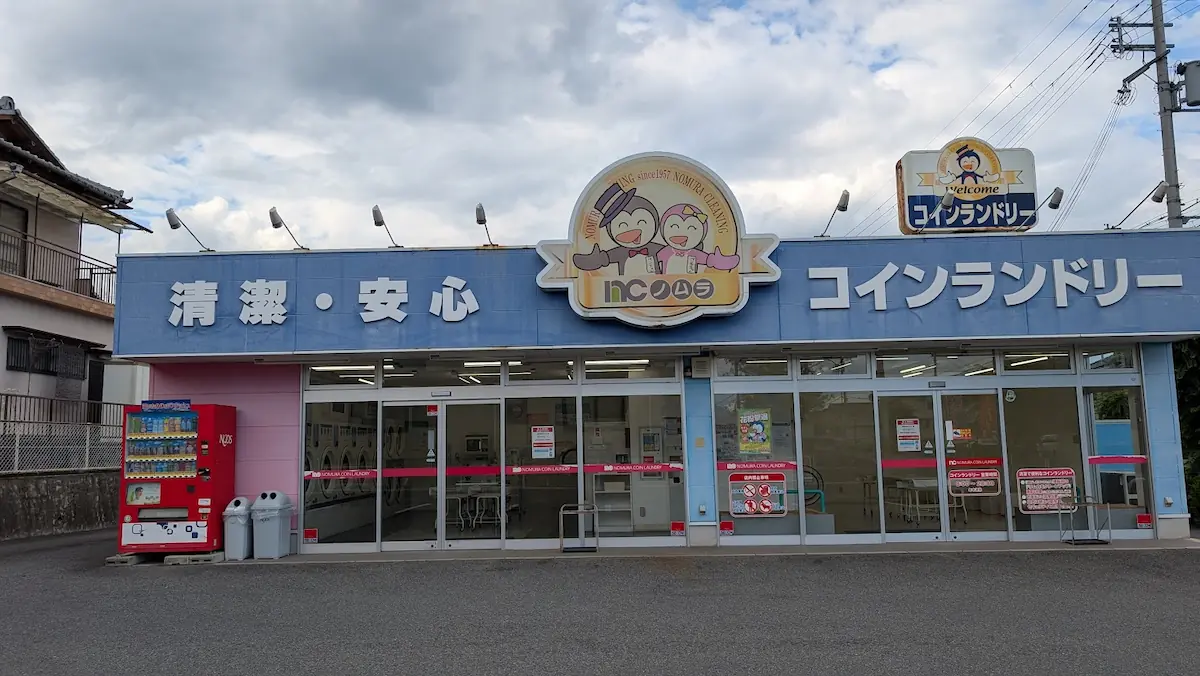 ノムラクリーニング コインランドリー真美ヶ丘店の正面。大きなガラス窓から店内の洗濯乾燥機が見え、清潔感のある店舗の様子
