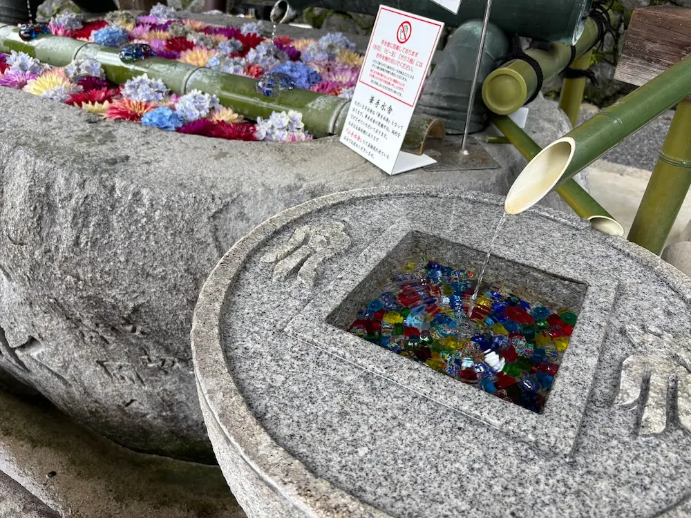 岡寺の手水舎の手前に置かれた、カラフルなビー玉が沈む小さな石の水鉢と流れ落ちる水