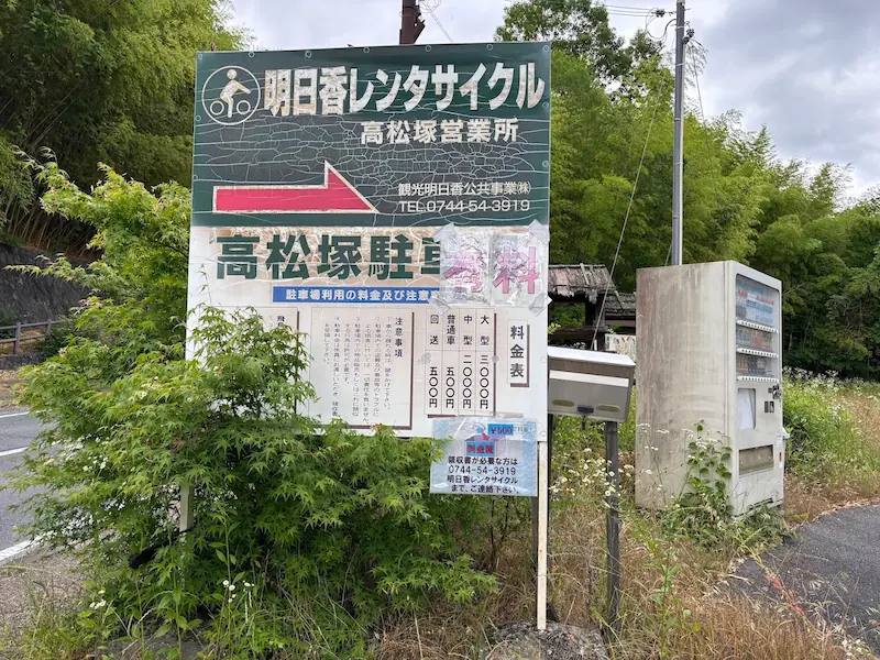 高松塚古墳周辺にある「明日香レンタサイクル高松塚営業所」の有料駐車場料金表が記載された看板