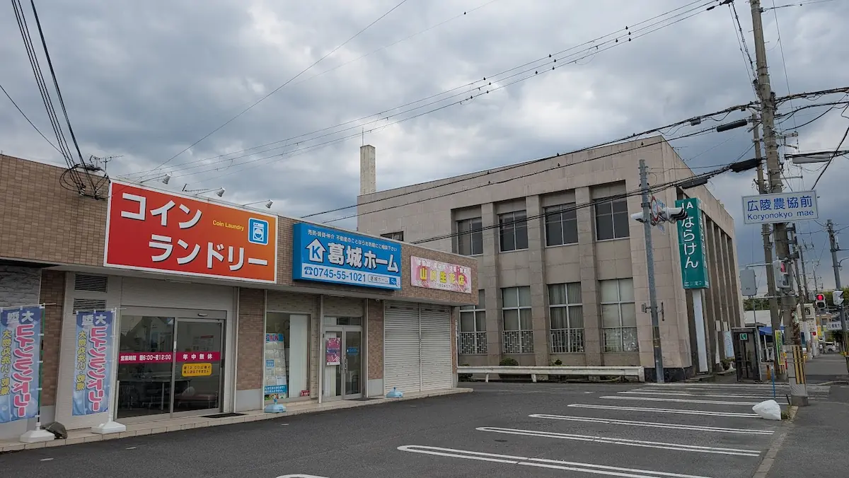 広陵町にあるコインランドリー「ウォッシュプラント」。オレンジ色の大きな看板が特徴で、周辺には不動産会社やJAが隣接している様子