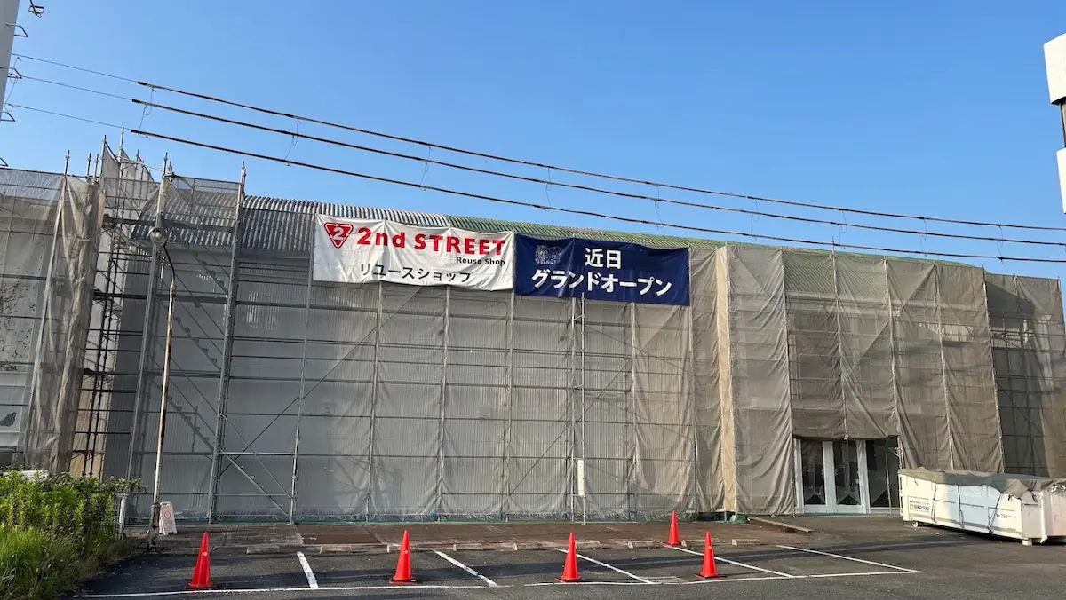 工事中の2nd STREET（セカンドストリート）の建物を正面から捉えた様子。足場とシートに覆われた外壁に「近日グランドオープン」の横断幕が掲げられ、手前には駐車スペースとコーンが置かれている。