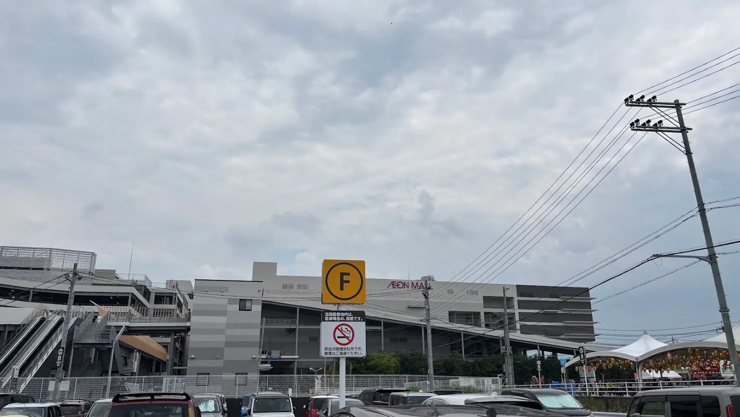 イオンモール橿原のウエストビレッジにある「F駐車場」の看板と、店舗建物の様子。雲の広がる空の下、施設へのアクセスが分かりやすい構図